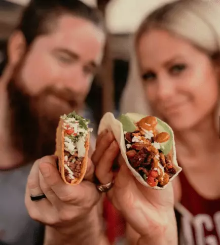 Two people hold tacos.